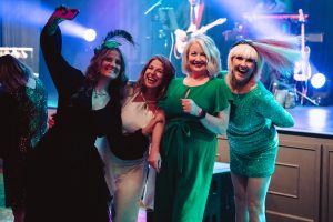 Four women on the dance floor in dresses and Oz themed attire. Hammers & High Heels 2024